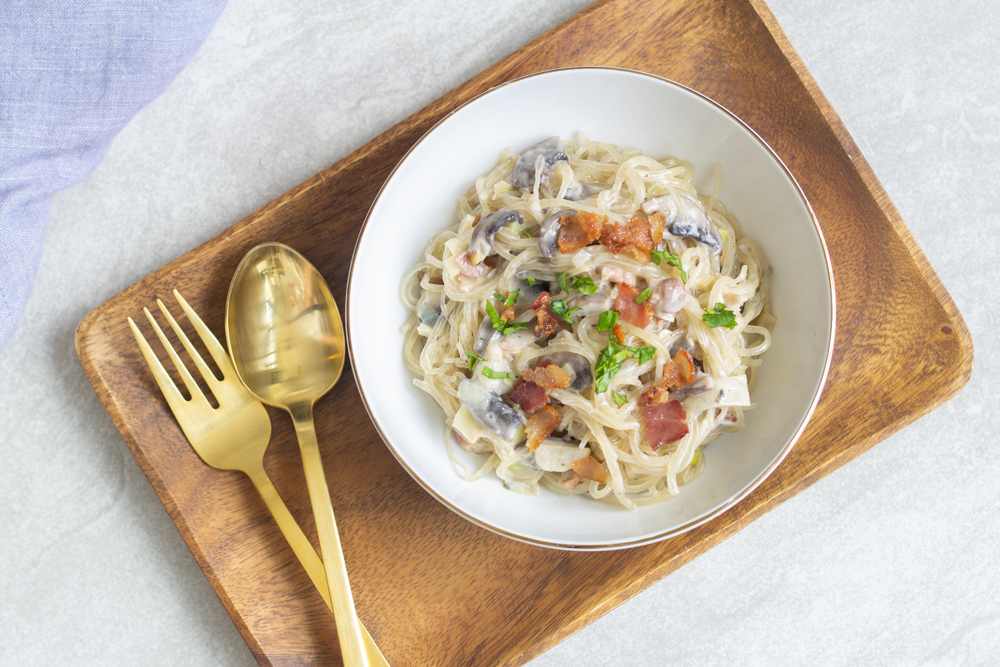 Bowl with spaghetti carbonara and crispy bacon on top.