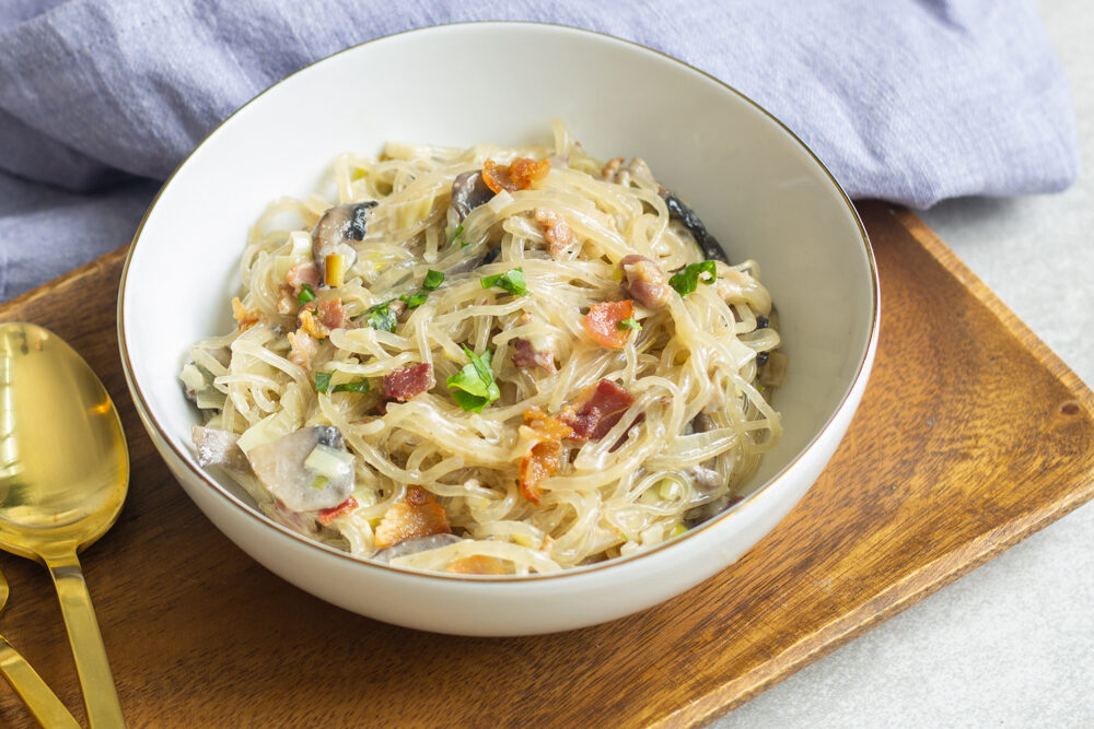 Bowl with spaghetti carbonara and crispy bacon on top.